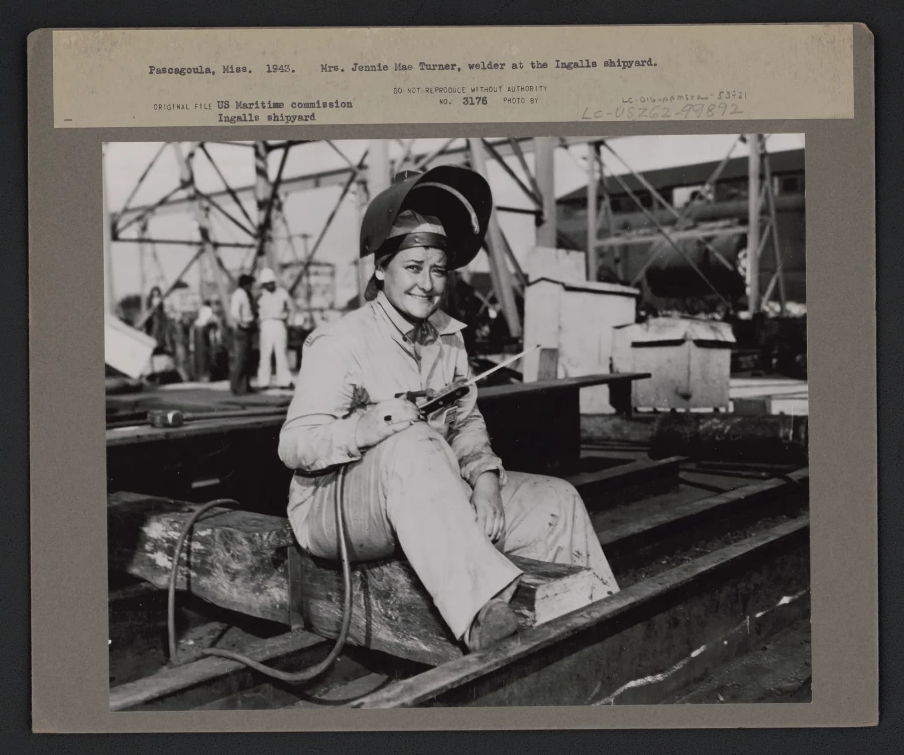 Archival mount holding a 1943 photograph of welder Jennie Mae Turner seated at the Ingalls shipyard in Pascagoula, with the typed caption slip visible above the print
